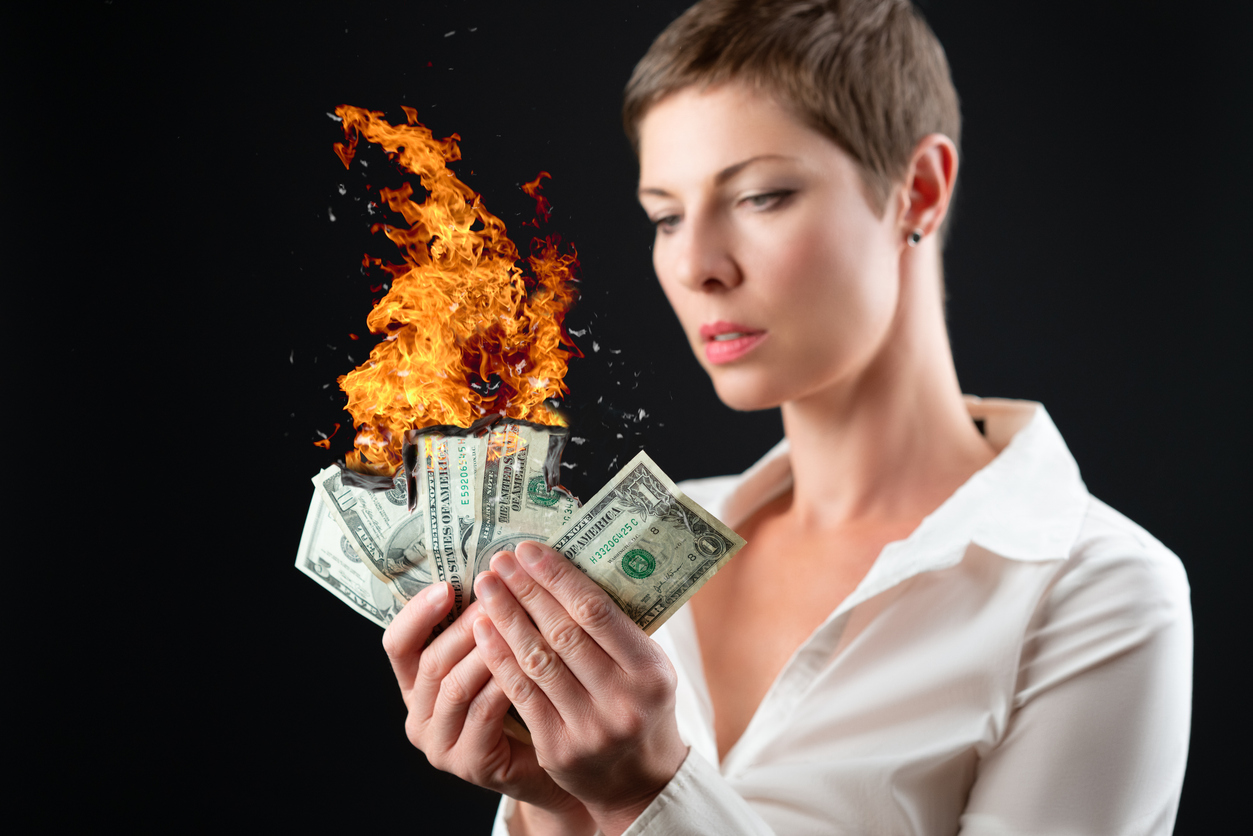 Short haired woman in white business shirt burning money on high out-of-pocket expenses, arising from health insurance mistakes.